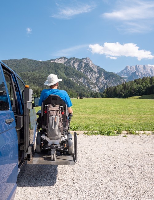 man gebruikt rolstoellift naast van, op vakantie in de bergen