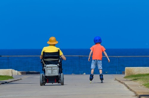papa in rolstoel met zoon op skates aan zee