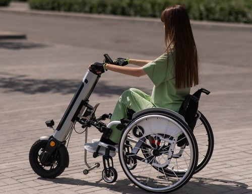 Een vrouw in een rolstoel met een hulpmiddel voor handmatige bediening. Elektrische handfiets.