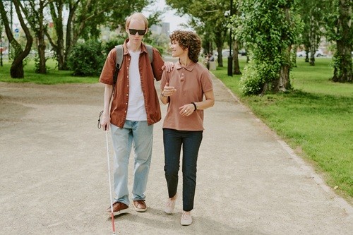 Man met visuele handicap met een vrouw die hem begeleidt.